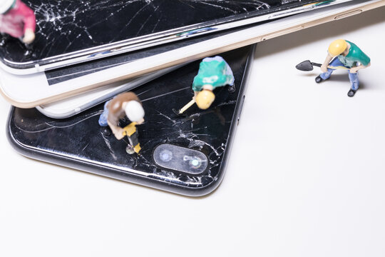 Miniature workers repairing cracked smartphones on white background