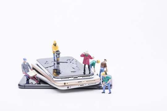 Miniature workers repairing cracked smartphones on stacked mobile phones
