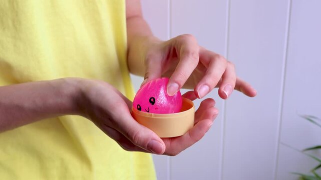 Close-up of hands opens package of pink dumpling shaped glitter squishy toy and then squeezing it during sensory play. Concept of stress relief, tactile activity, relaxation and emotional balance.