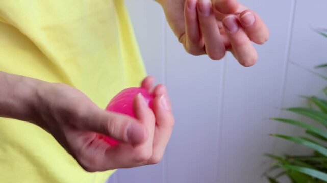 Close-up of hands holding and squeezing a pink dumpling shaped glitter squishy toy during sensory play. Concept of stress relief, tactile activity, relaxation and emotional balance.