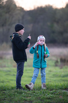 Children enjoy a playful afternoon in a serene green field as they blow colorful bubbles while the sun sets in the background, creating a magical moment together
