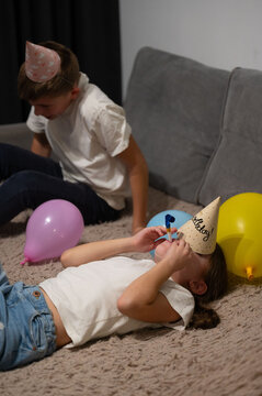 Children celebrating a birthday party indoors while wearing colorful hats and playing with balloons in a cozy living room during the evening hours
