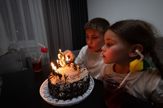 Celebrating a special moment with joyful kids blowing out candles on an elegant chocolate cake during a cozy indoor birthday party at night