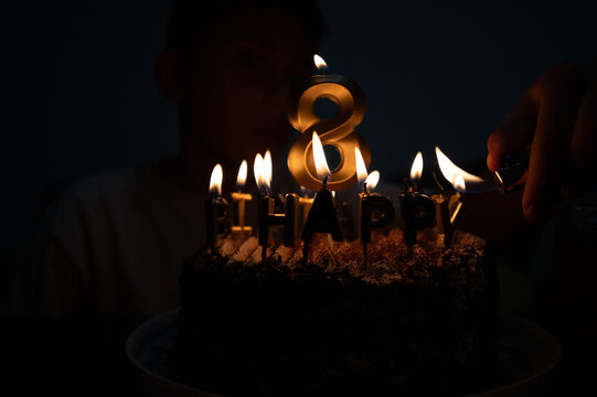 Celebrating a special birthday with candles and laughter as a young boy prepares to blow out the flames on a delicious chocolate cake adorned with the number eight