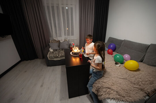 Children celebrating a joyful birthday with cake and colorful balloons in a cozy bedroom during an evening gathering among friends and family