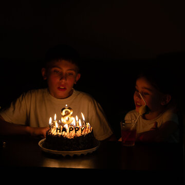 Children celebrating a birthday with a chocolate cake adorned with candles in a dimly lit room, creating a warm and joyful atmosphere during a cherished moment