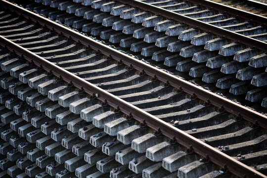 Close-up of parallel railway tracks with concrete sleepers, repeating pattern of rail lines and ballast stones, shallow depth of field