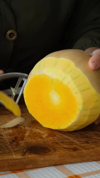 Vertical video. Person peeling pumpkin. Preparing autumn food. Cooking pumpkin soup or cake.