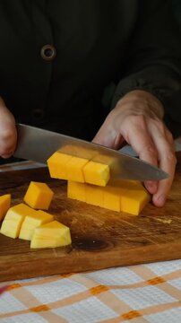 Vertical video. Female hands slicing pumpkin. Preparing autumn food. Cooking pumpkin soup or cake.