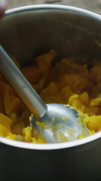 Vertical video. Cooking pumpkin puree soup. Mixer mashes cooked pumpkin in pot