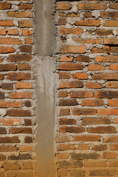 Vertical close up of Unfinished red clay brick wall texture with concrete mortar and cement pillar. Construction background with rough masonry surface. Ideal for building and architecture concepts