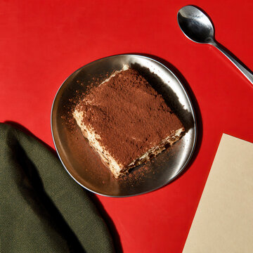 Tiramisu dessert served in a black bowl on a bold red table