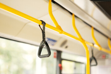 Black grab handle strap hanging on yellow handrail in public transport interior. Safety equipment for standing passengers in city bus, train, or tram. © Aigul Sabirova