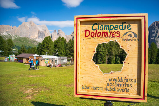 Ciampedie, Italy - July 16, 2026: Wooden tourist photo frame and Ciampedie Dolomites sign standing in a green alpine meadow with spectacular mountain peaks in the background