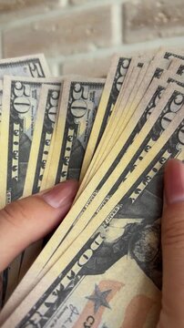 Woman's hands holding and counting a large stack of fifty dollar bills, representing financial success, wealth, income, and the concept of making and spending money