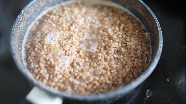 Buckwheat groats boiling and bubbling in a small saucepan on a kitchen stove during home cooking