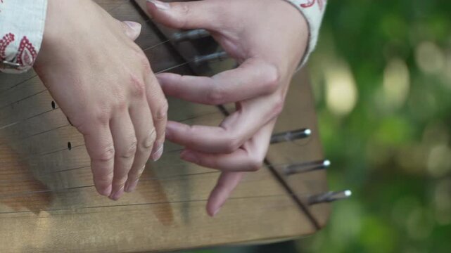 Instrument playing folk, close-up hands playing traditional string instrument outdoors