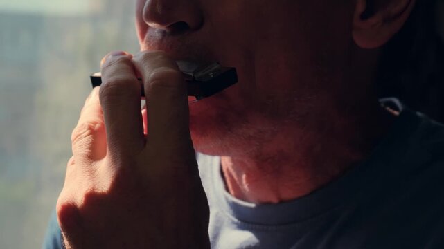 Close-up of a middle-aged man playing the harmonica at home.