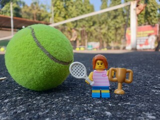 Obraz premium Indonesia - August 31, 2024 : Mini toy of action figure at tenniscourt with blurred background. Sport photography concept design. Miniature Young girl with trophy and tennis racket. Winning athlete.