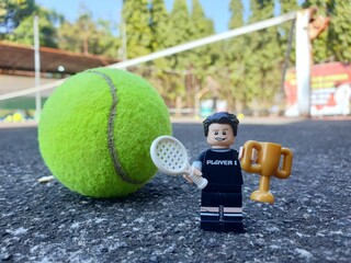 Obraz premium Indonesia - August 31, 2024 : Mini toy of acrion figure at tenniscourt with blurred background. Sport photography concept design. Young man athlete at tennis club.