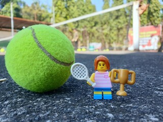 Obraz premium Indonesia - August 31, 2024 : Mini toy of action figure at tenniscourt with blurred background. Sport photography concept design. Miniature Young girl with trophy and tennis racket. Winning athlete.