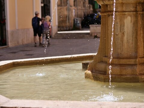 Water Splashing in Stone Fountain with People Walking BehindExplanation: Dynamic shot of water trickling into a stone fountain basin with pedestrians blurred in the sunny background.