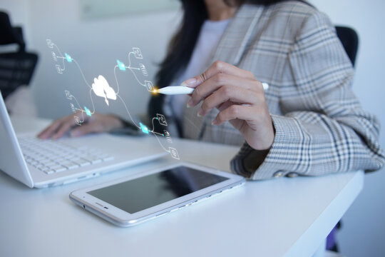 Businesswoman Pointing Stylus Pen At Cloud Diagram While Using Laptop On Office Desk