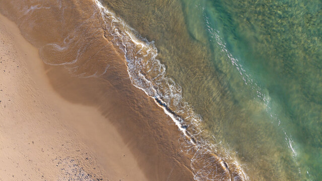 Aerial view of the sandy shoreline and turquoise waves crashing on Dee Why Beach in Dee Why, New South Wales, Australia.