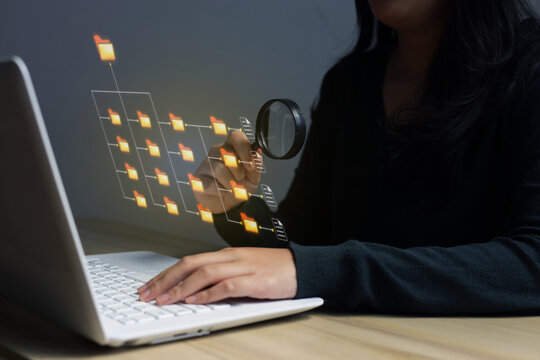 Close Up Of Hand Inspecting Folder Structure With Magnifying Glass In Front Of Laptop