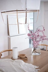 Fototapete Japandi minimalist interior, dining room, dining table, cherry blossom, blossom branches, spring flowers, floral arrangement, glass vase, wooden table, Scandinavian interior, Japandi, minimal home, home decor  © Natalie