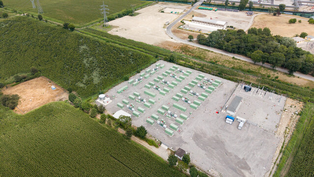 Aerial view of BESS SERRE TAVAZZANO battery energy storage system with rows of green containers on a gravel lot surrounded by agricultural fields in Tavazzano con Villavesco, Lombardy, Italy.