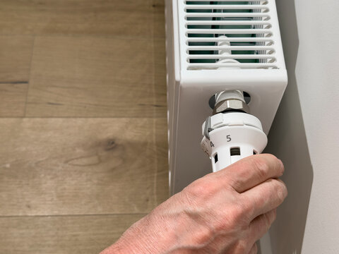 Hand adjusts a thermostatic radiator valve on a white heater. Home heating control for temperature regulation and energy saving. Indoor maintenance in a modern interior..