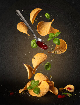 Potato chips falling with ketchup, basil leaves and spices on black background