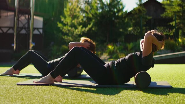 Elderly women practicing slow motion Pilates on foam rollers outdoors, focusing on gentle core strengthening, flexibility, balance, and mindful senior fitness