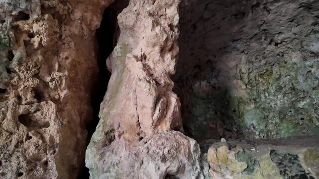 Xemxija, Malta 29.07.2026 - Heritage trail, Roman Baths, shelf like cut in the stone Dark cave walls show rough, textured surfaces. Greenish moss grows on damp, uneven stone. Light filters through nar