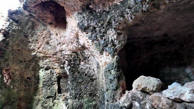 Xemxija, Malta 29.07.2026 - Heritage trail, Roman Baths, shelf like cut in the stone Dark cave walls show rough, textured surfaces. Greenish moss grows on damp, uneven stone. Light filters through nar