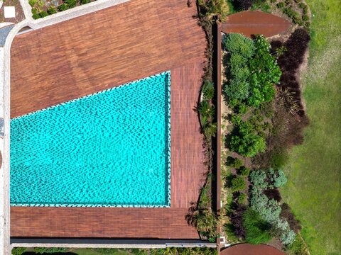 Aerial view of a turquoise swimming pool surrounded by wooden decking and lush garden landscaping in Cascais, Porto, Portugal.