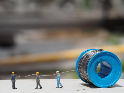 Mini toy of action figure at outdoor with blurred background. Miniature photography concept design. Minifigure of engineer character with induatrial cable. Site plant, Industry and factory situation.
