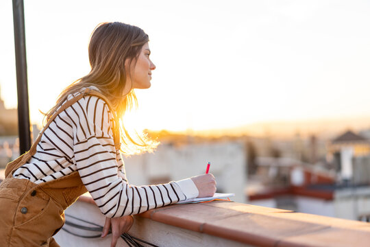 Young woman taking notes on roof terrace at sunset