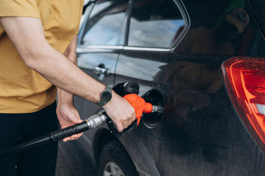 Hands holding pump nozzle to refuel a black car