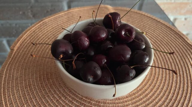 Fresh ripe dark cherries in a white bowl on a woven placemat, healthy summer fruit snack and juicy vitamin rich dessert for a natural vegan lifestyle and diet