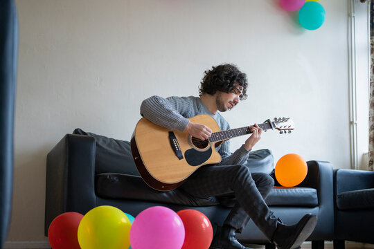 Young man playing guitar while sitting on sofa at home