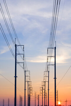 Silhouette two rows of electric poles with cable lines in countryside area against sunset sky background in vertical frame