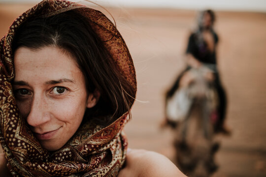 Smiling traveler in scarf at Sahara desert with camel rider