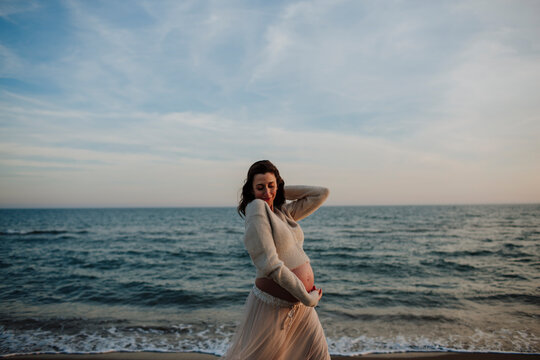 Pregnant woman dancing on the beach at sunset