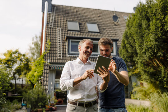 Happy father and son using digital tablet while standing in backyard