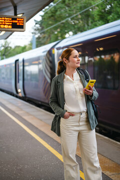 Businesswoman waiting for train on platform holding smartphone
