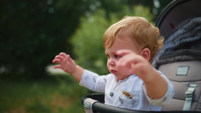 Cute toddler in stroller gazes at floating bubbles. Child's hands reach toward colorful spheres. Gentle smile shows pure joy and wonder. Perfect for family, childhood, or summer-themed content