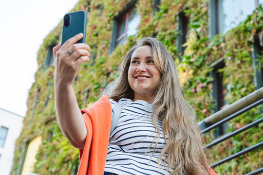 Smiling woman takes a selfie in front of a green building