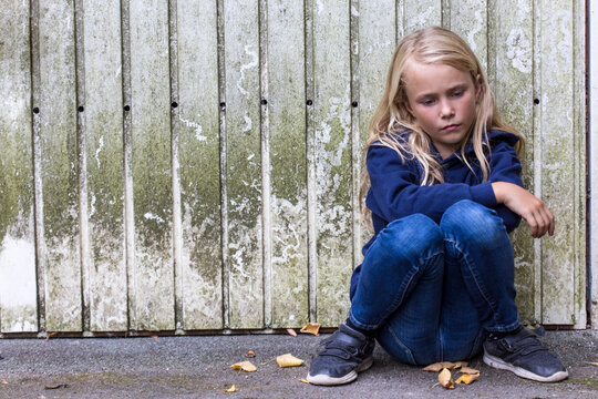 Portrait of sad girl sitting in front of wooden wall